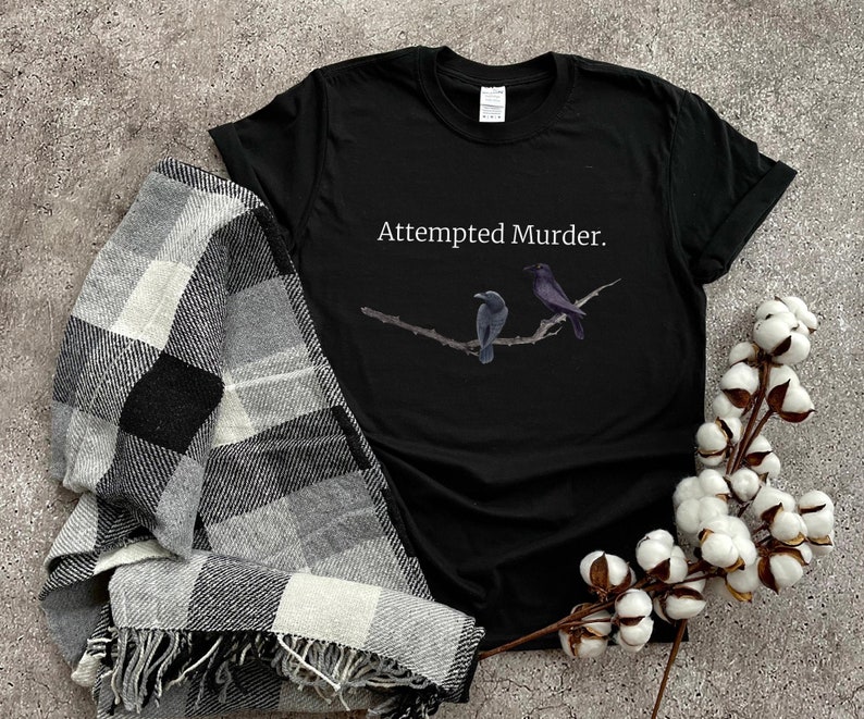Puede incluir: Camiseta negra con el texto "Attempted Murder." y un gr&aacute;fico de dos p&aacute;jaros negros en una rama.