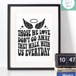 May include: Black and white print with the text "Those we love don't go away they walk with us everyday" in a retro font. The print features a pair of angel wings with a halo above them and a heart.