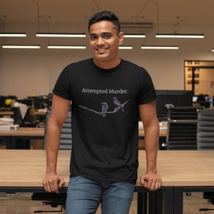 Puede incluir: Una camiseta negra con el texto "Attempted Murder." impreso en la parte delantera. La camiseta presenta un gr&aacute;fico de dos p&aacute;jaros posados en una rama.
