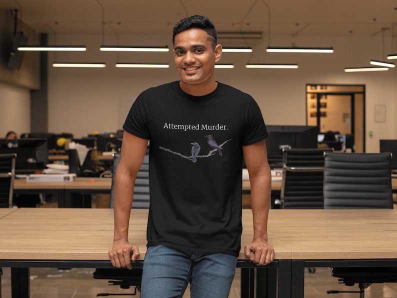 Puede incluir: Una camiseta negra con el texto "Attempted Murder." impreso en la parte delantera. La camiseta presenta un gr&aacute;fico de dos p&aacute;jaros posados en una rama.
