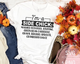 Puede incluir: Camiseta blanca con texto negro que dice "I'm-a SIDE CHICK: MASHED POTATOES, STUFFING, GREEN BEAN CASSEROLE, GRAVY, BRUSSEL SPROUTS, CRANBERRY SAUCE". La camiseta está sobre una superficie de madera con pantalones vaqueros azules y follaje de otoño.