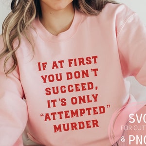 May include: Pink sweatshirt with the text "IF AT FIRST YOU DON'T SUCCEED, IT'S ONLY "ATTEMPTED" MURDER" in red.