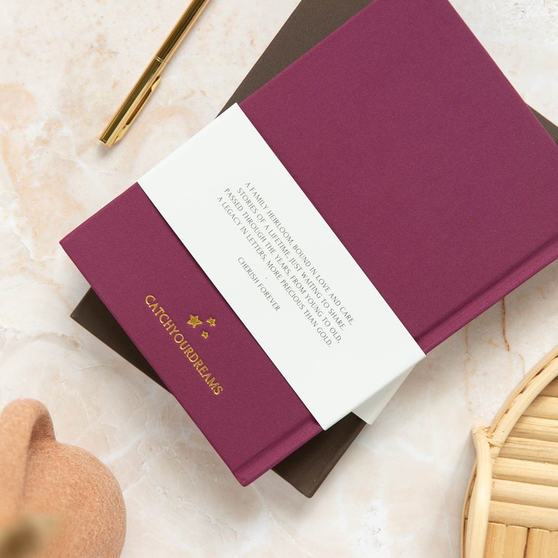 May include: A burgundy journal with a white band that reads "A family heirloom bound in love and care, stories of a lifetime, just waiting to share. Passed through the years, from young to old, a legacy in letters, more precious than gold. Cherish forever." The journal has gold stars and the text "Catchyourdreams" printed on the front cover.