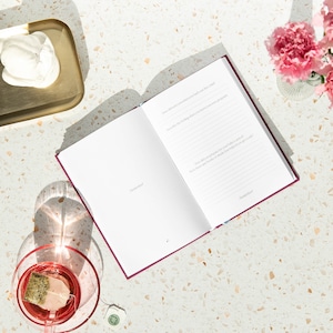 May include: An open burgundy journal with lined pages and the text "How did you know when you had met your child?" and "How did you prepare for your baby's arrival? What are the books or items that helped you the most?"