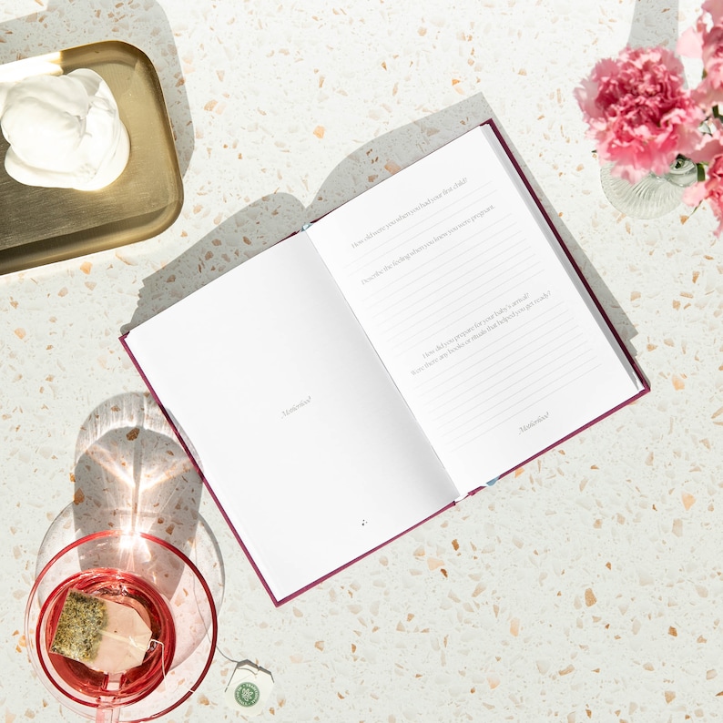 May include: An open burgundy journal with lined pages and the text "How did you know when you had met your child?" and "How did you prepare for your baby's arrival? What are the books or items that helped you the most?"