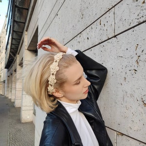 Könnte beinhalten: Eine Frau mit blonden Haaren trägt ein weißes Hemd und eine schwarze Lederjacke. Sie trägt ein gehäkeltes Stirnband mit Blumenmuster.