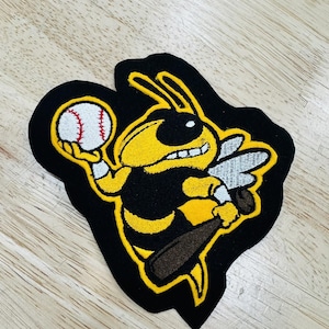 Puede incluir: Parche bordado con un avispa amarilla y negra de estilo caricatura sosteniendo una pelota de béisbol y un bate. La avispa tiene una expresión decidida. El parche está contorneado en amarillo y tiene un fondo negro.