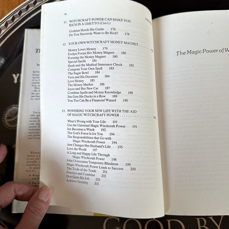 K&ouml;nnte beinhalten: Ein Buch mit dem Titel "The Magic Power of Witchcraft" mit einem schwarzen und wei&szlig;en Umschlag. Das Buch ist auf einer Seite ge&ouml;ffnet, auf der eine Liste von Kapiteln mit den Titeln "Witchcraft Power Can Make You Rich in a Ghetto" und "Powering Your New Life with the Aid of Magic Witchcraft Power" steht.