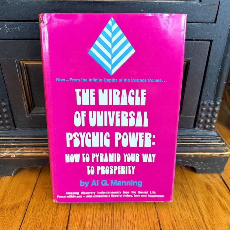 May include: A vintage book titled "The Miracle of Universal Psychic Power" by Al G. Manning. The book has a bright pink cover with white text and a blue and white geometric design. The book's cover also includes additional text.