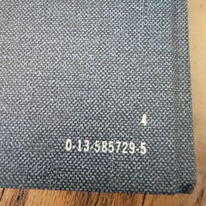 May include: Close-up of a gray woven fabric with a subtle pattern. The fabric has a textured appearance and a small white symbol. The number "4" is next to the symbol. The text "0-13-585729-5" is printed on the fabric.