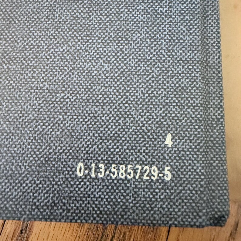 May include: Close-up of a gray woven fabric with a subtle pattern. The fabric has a textured appearance and a small white symbol. The number "4" is next to the symbol. The text "0-13-585729-5" is printed on the fabric.