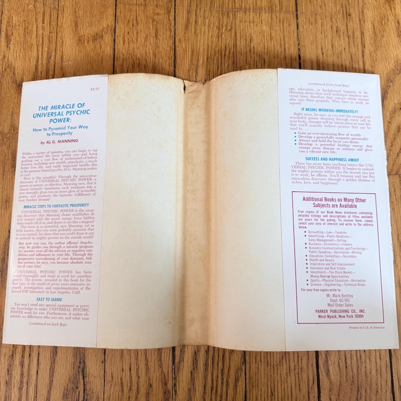 May include: An open book with the title "The Miracle of Universal Psychic Power" by A.G. Manning. The book's pages are aged, with text on the left and right pages. The cover is white with black text. The book is on a wooden surface.