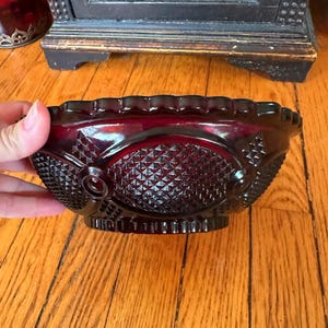 Könnte beinhalten: Eine tiefrote Glasschüssel mit einem Diamantenmuster und einem gewellten Rand. Die Schüssel ist aus rubinrotem Glas und hat einen Vintage-Look.
