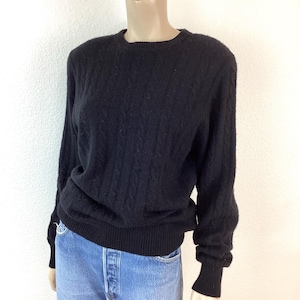 May include: A black cable knit sweater with long sleeves and a crew neck.