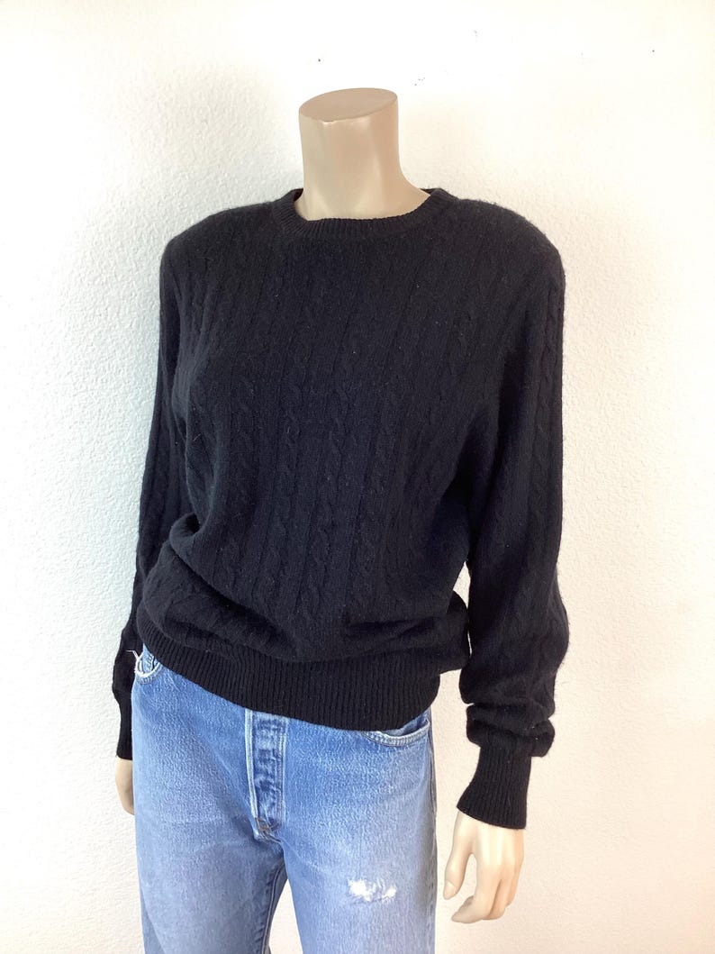 May include: A black cable knit sweater with long sleeves and a crew neck.