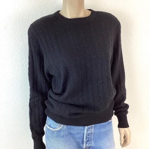 May include: A black cable knit sweater with long sleeves and a crew neck.