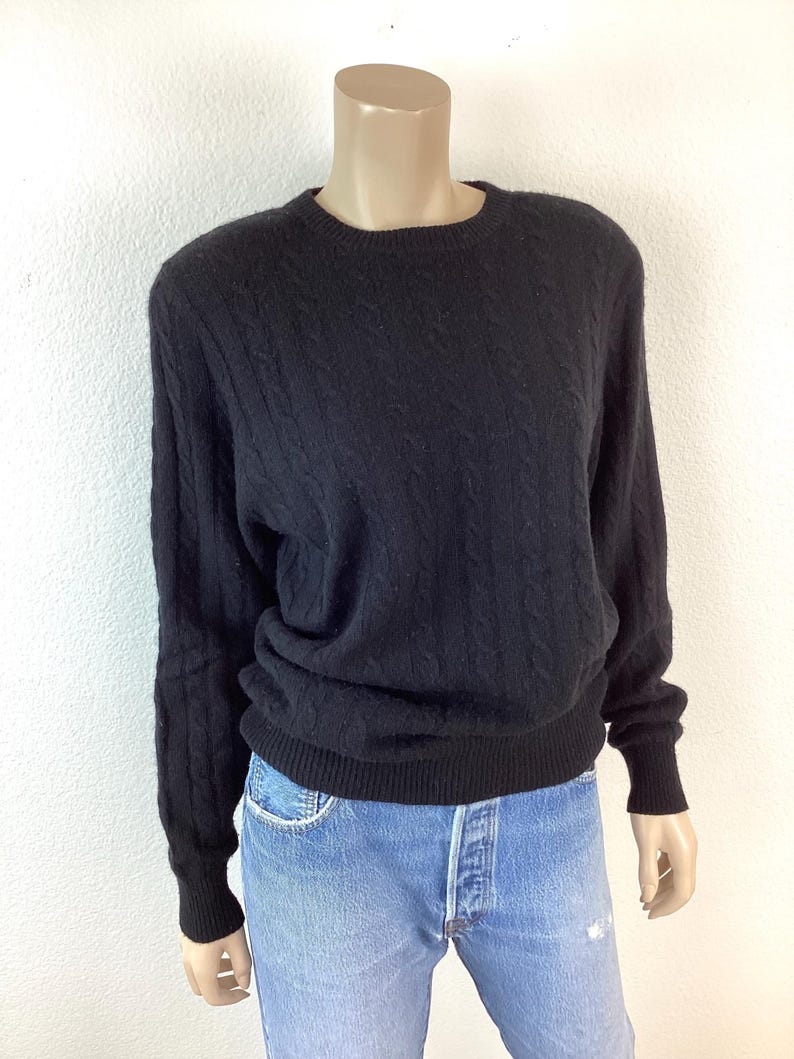May include: A black cable knit sweater with long sleeves and a crew neck.