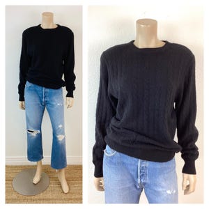 May include: A black cable knit sweater with a crew neck. The sweater is shown on a mannequin wearing blue jeans.