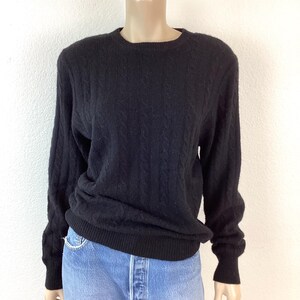 May include: Black cable knit sweater with long sleeves and a crew neck.