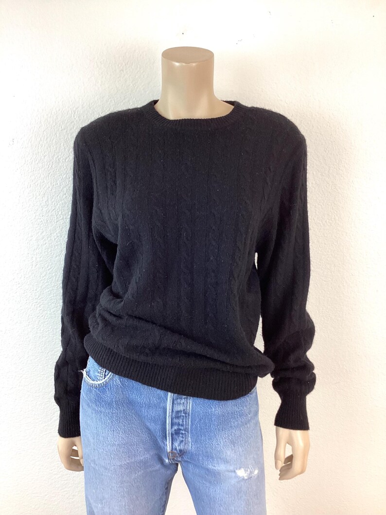 May include: Black cable knit sweater with long sleeves and a crew neck.