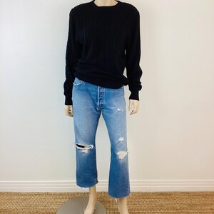 May include: A black long-sleeved sweater with a crew neck and a pair of light blue distressed jeans.