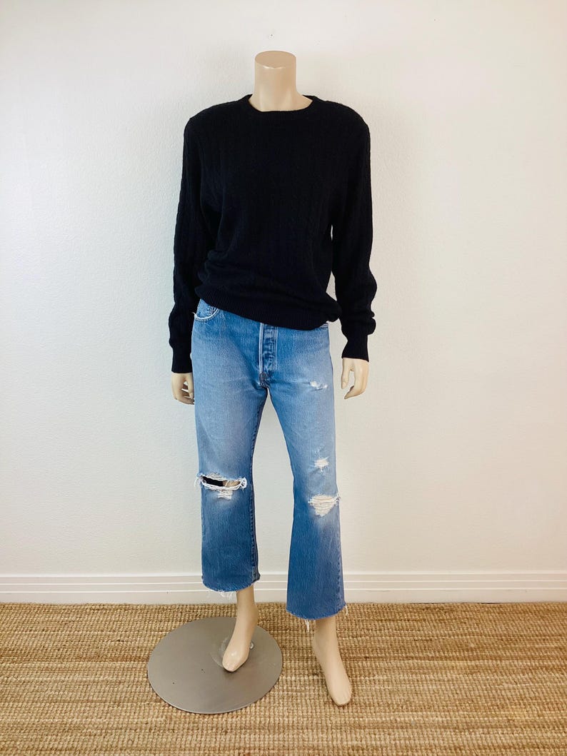 May include: A black long-sleeved sweater with a crew neck and a pair of light blue distressed jeans.