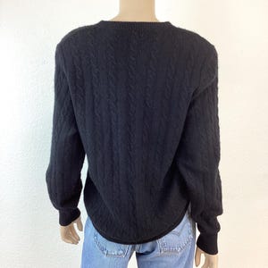 May include: Black cable knit sweater with a crew neck. The sweater is made of a soft, comfortable material.