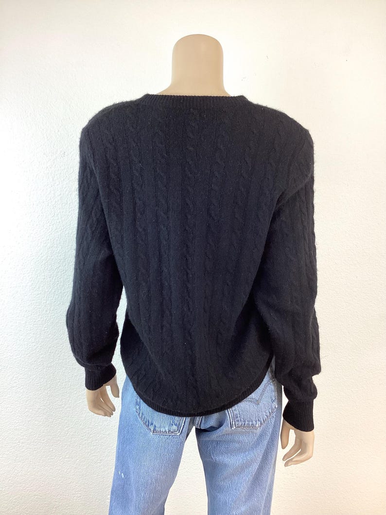 May include: Black cable knit sweater with a crew neck. The sweater is made of a soft, comfortable material.