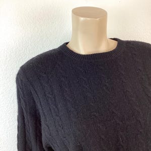 May include: A black cable knit sweater with a crew neck.