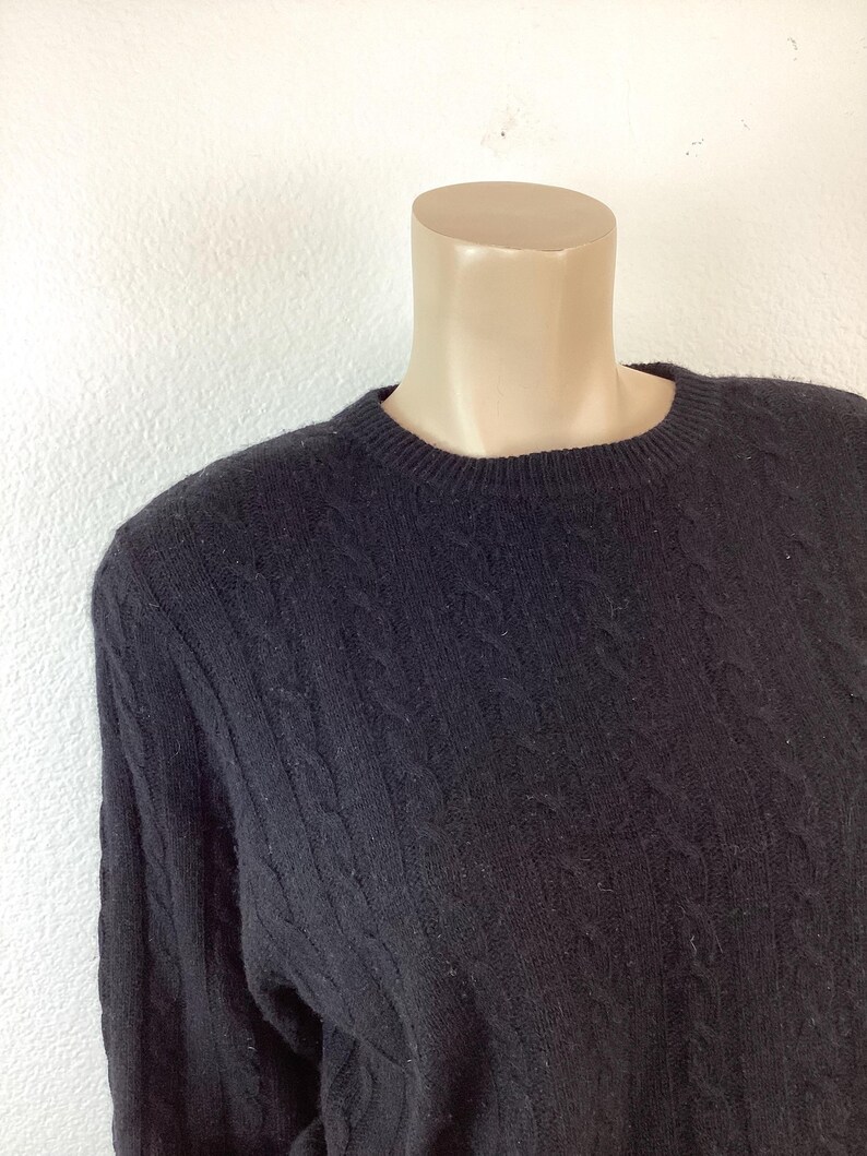 May include: A black cable knit sweater with a crew neck.