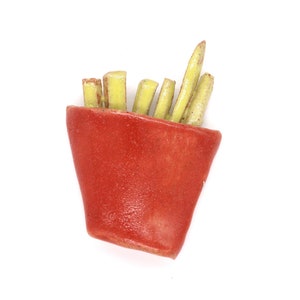 May include: A red ceramic container filled with yellow ceramic french fries.