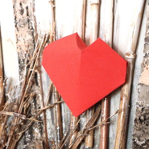 May include: A red paper heart is placed against a background of white and brown wooden sticks.
