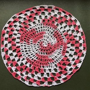 Könnte beinhalten: Eine gehäkelte Tischdecke in Rosa und Weiß mit einem Spiralmuster.