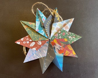 May include: A multi-colored paper star ornament with a string for hanging. The star is made of 12 points and is decorated with various patterns, including animals, plants, and geometric designs.