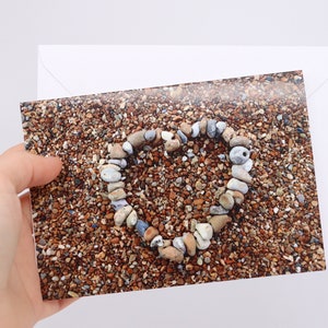 May include: A heart shape made of small stones on a beach of small pebbles.