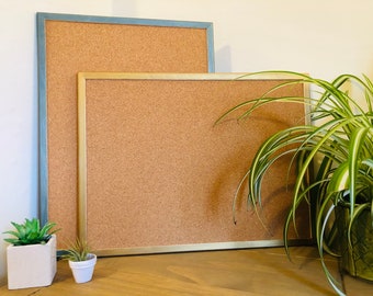 Op de afbeelding: Twee kurk borden met frames. Het grotere bord heeft een blauwe frame en het kleinere bord heeft een gouden frame. Beide borden staan op een houten oppervlak.