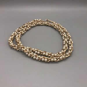May include: A gold chain necklace with faux pearls. The chain is woven with the pearls.