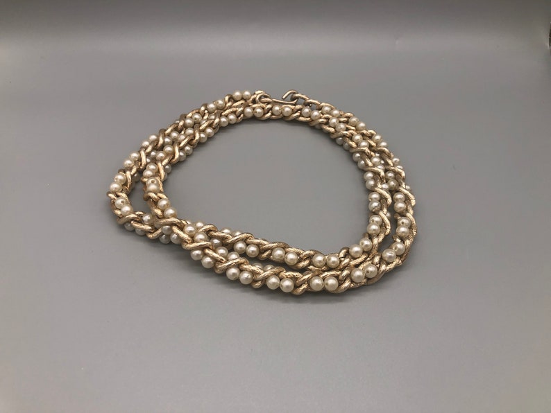 May include: A gold chain necklace with faux pearls. The chain is woven with the pearls.