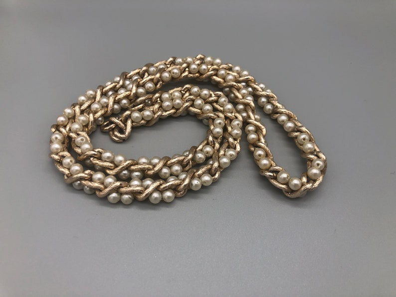 May include: A gold chain necklace with faux pearls woven into the chain.