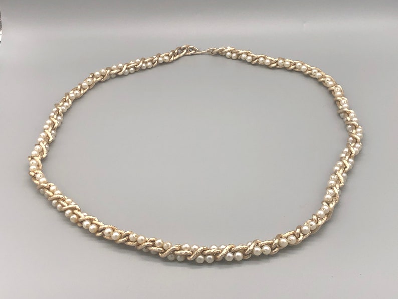 May include: A gold chain necklace with white faux pearls woven into the chain.
