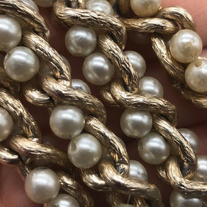 May include: A gold chain necklace with faux pearls. The chain is textured and the pearls are white.