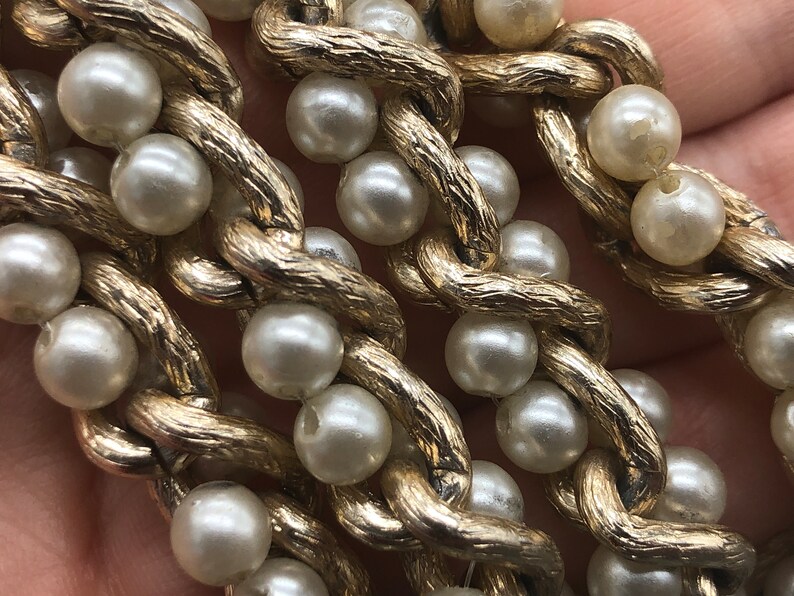 May include: A gold chain necklace with faux pearls. The chain is textured and the pearls are white.