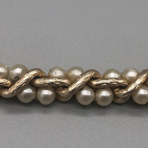 May include: A gold chain with faux pearls, the chain is woven in a pattern that resembles a braid.