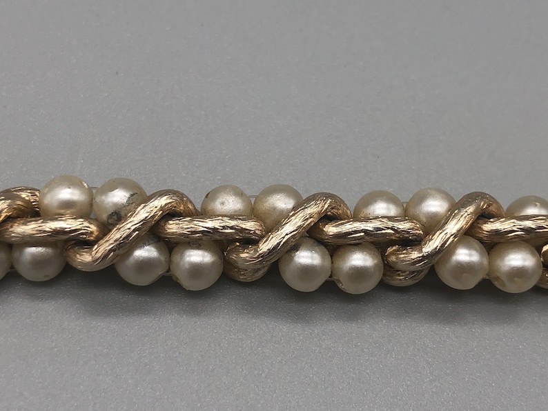 May include: A gold chain with faux pearls, the chain is woven in a pattern that resembles a braid.