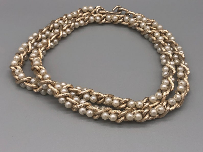 May include: A gold-tone necklace with a braided chain design and faux pearl accents.