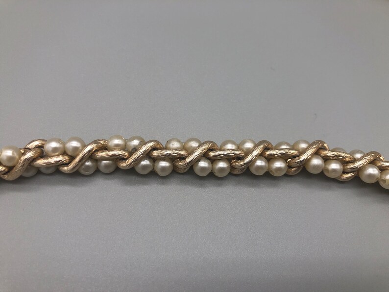 May include: A gold chain necklace with faux pearls woven into the chain.