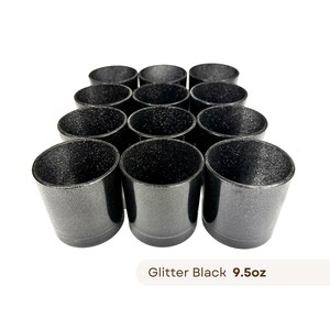 Może przedstawiać: Dwunastu czarnych kubków z błyszczącym wykończeniem. Kubki są ułożone w kształcie piramidy. Tekst "Glitter Black 9.5oz" jest nadrukowany pod kubkami.