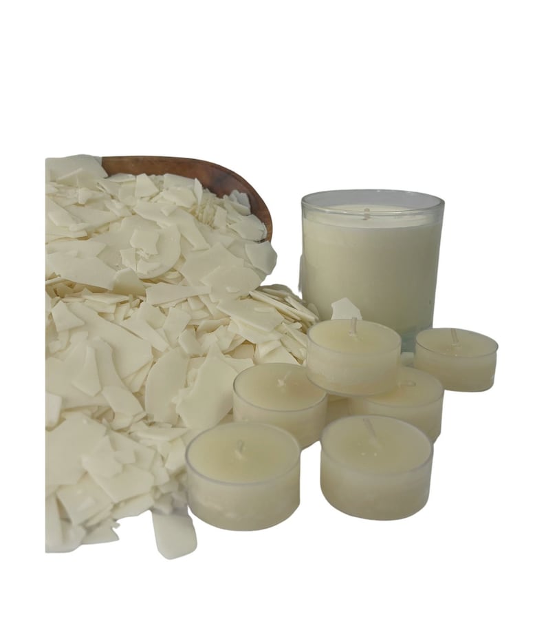 May include: A close-up of white wax flakes, a large white candle in a glass jar, and several small white tea light candles. The wax flakes are in a wooden bowl.