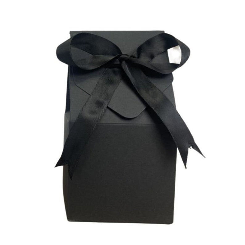 May include: A black gift box with a black satin ribbon tied in a bow. The box is made of sturdy cardboard and has a flap on the top.