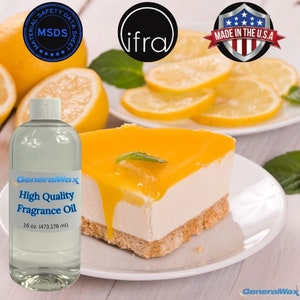 May include: A clear glass bottle with a white label that reads "GeneralWax High Quality Fragrance Oil 16 oz. (473.176 ml)". The bottle is sitting on a white surface with a slice of lemon cheesecake and lemon slices in the background.